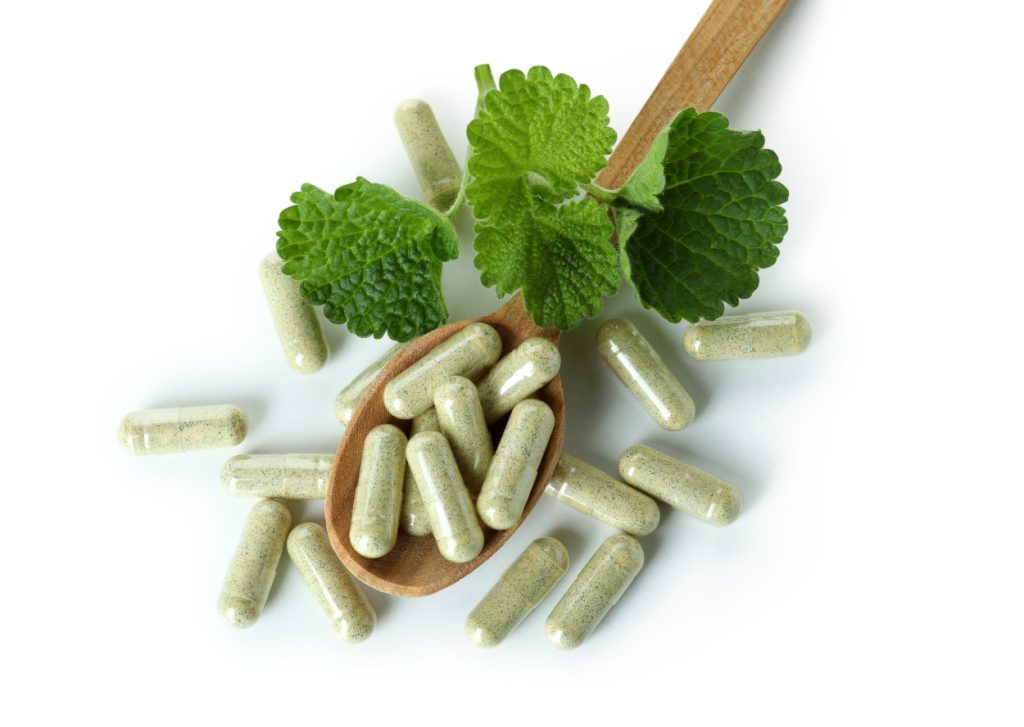 Food suplements. Area of expertise. Green pills with herbals lay on the big wooden spoon. White background.