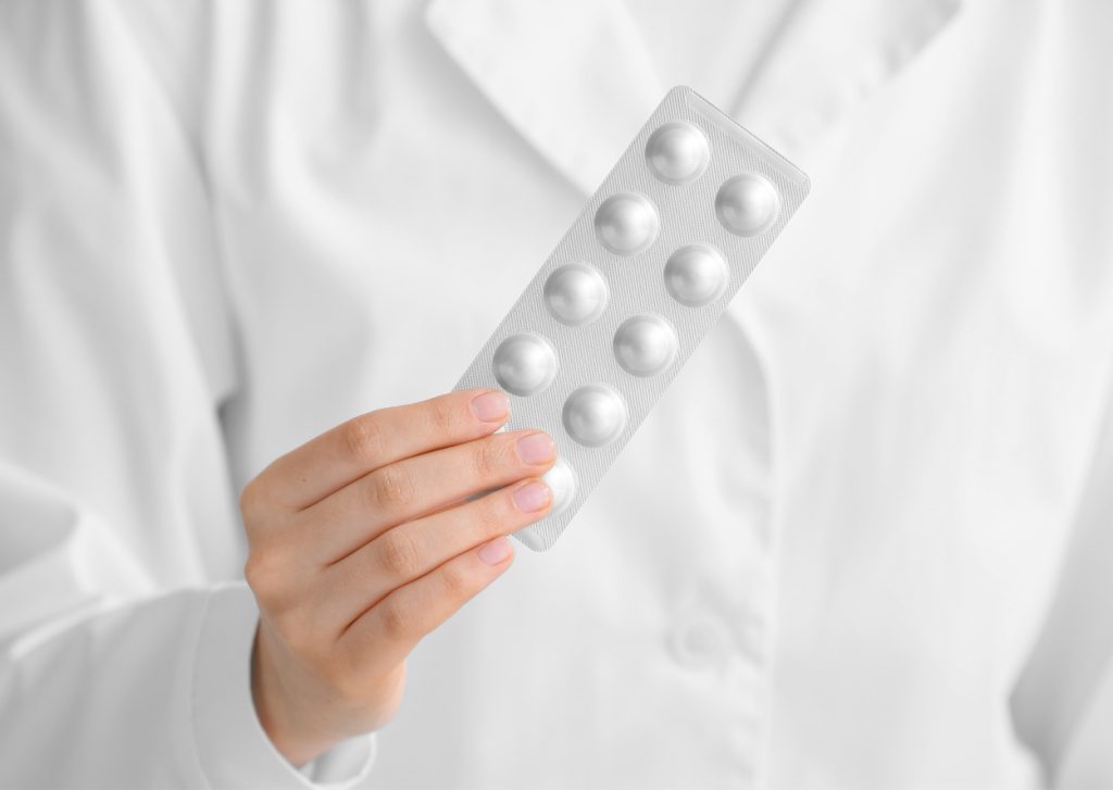 IMP. Person in white suit hold some pills blister in their own.
