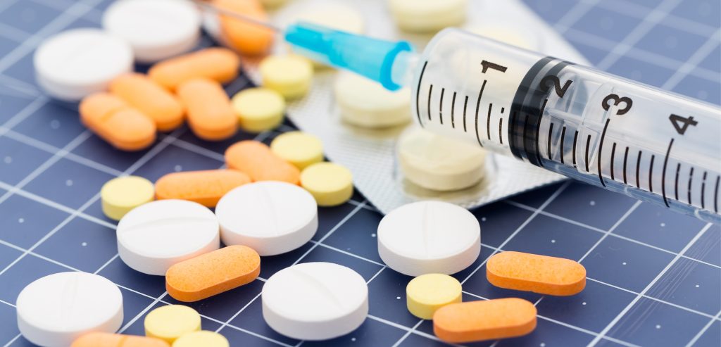 Medicinal products. White, yellow, orange pills on blue background. Syringe with a needleabove them.