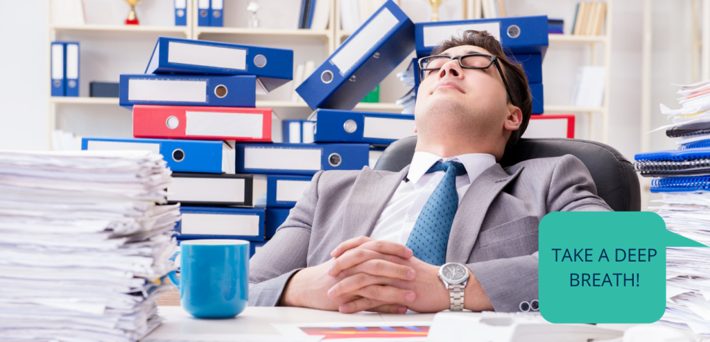 Exhausted man in an office, overwhelmed by piles of documents while preparing the medical part of a registration dossier.