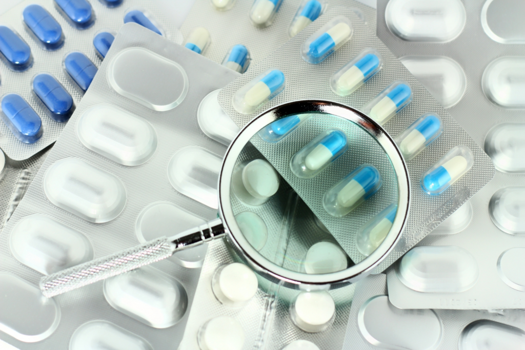 Close-up of a magnifying glass on a blister pack of tablets, symbolizing the detailed pharmacovigilance inspection process, ensuring drug safety compliance and regulatory adherence.
