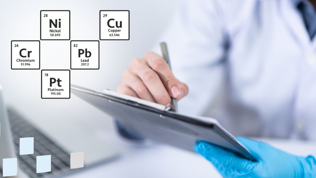Symbols of chemical elements in the foreground with hands, a pen, a notepad, and a computer keyboard in the blurred background, representing the assessment and control of elemental impurities (EI) in medicinal products according to the ICH Q3D Guideline. The image reflects the importance of managing EI levels to comply with regulatory standards and ensure product safety.