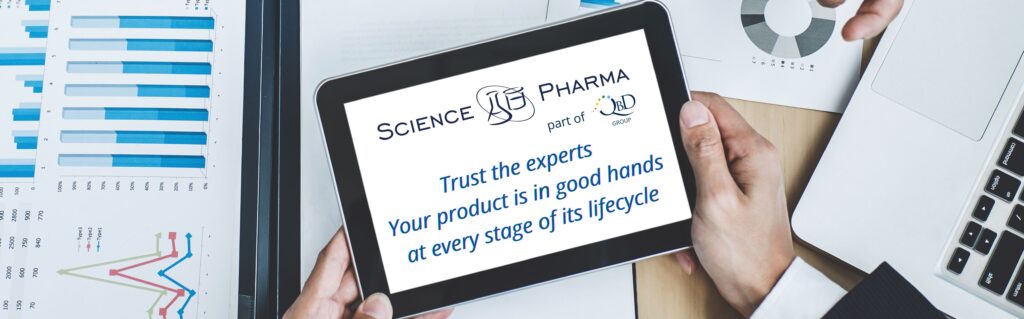In the foreground, hands are holding a tablet displaying the phrase “Trust the experts” and the SciencePharma by QbD logo. In the background, there is a stack of documents symbolizing regulatory analysis, compliance documentation, and data audits. The image conveys professional expertise, structured support in xEVMPD data management, and regulatory reliability under EMA, GVP, and ISO IDMP frameworks.